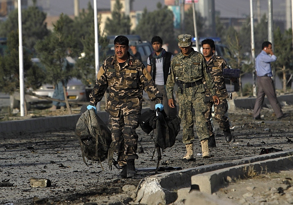 Afghan security personnel carry bags belonging to foreign contractors at the site of a suicide attack