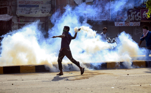 A protester throws a teargas canister, which was thrown by the police earlier, during clashes in Lahore