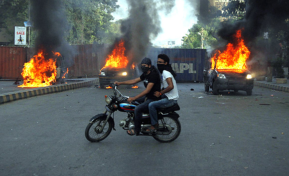 Protesters ride past burning police vehicles during an anti-American protest rally to mark the 'Day of Love' in Karachi