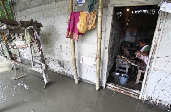 A flood affected woman prepares food inside her submerged hut at Lachi Bishnupur village in Assam