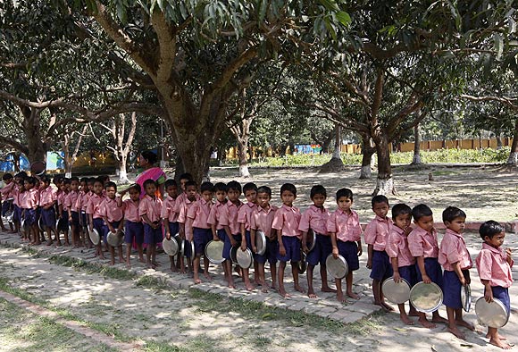 Children stand in line to collect their free mid-day meal in a school