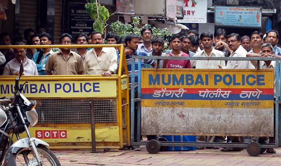 Onlookers stand behind a barricade installed by police at Zaveri Bazaar