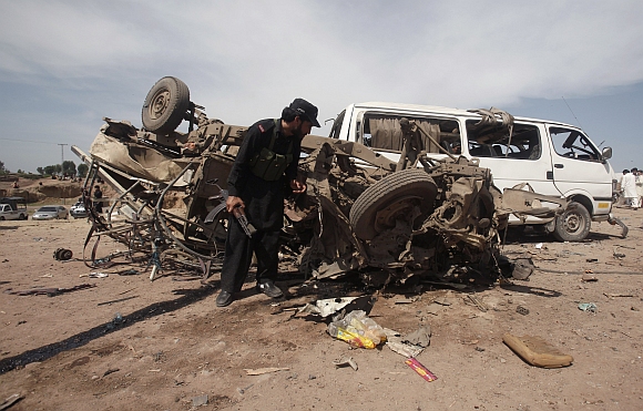 A security official inspects a damaged vehicle at the site of a bomb attack near Jalozai camp in Nowshera district, northwestern Pakistan