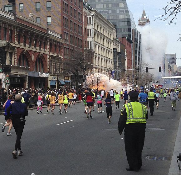 Runners continue to run towards the finish line of the Boston Marathon as an explosion erupts near the finish line of the race in this photo exclusively licensed to Reuters by photographer Dan Lampariello after he took the photo