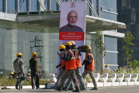 Workers walk past a poster of Gujarat's Chief Minister Narendra Modi installed at the construction site of Gujarat International Finance Tec-City (GIFT) building at Gandhinagar