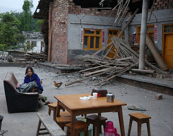 A woman sits outside a heavily damaged building in the Gonghe village