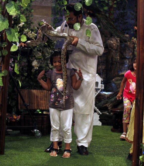 Aamir Liaquat Hussain, host of the Geo TV channel programme 'Amaan Ramazan', puts a snake around a child's shoulders during a live show in Karachi