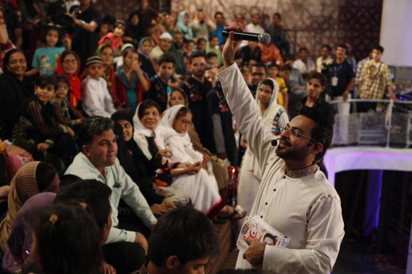 Aamir Liaquat Hussain waves a microphone while asking participants questions during a live show in Karachi