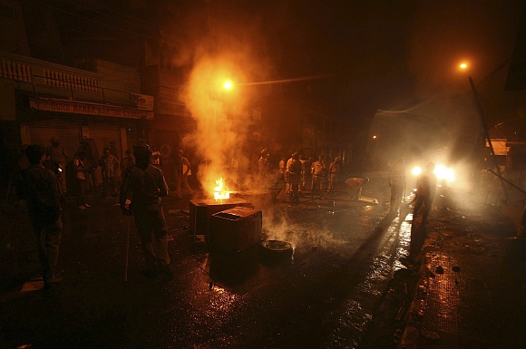 Policemen stand guard by burning debris after shops were set afire by a mob in Jammu 