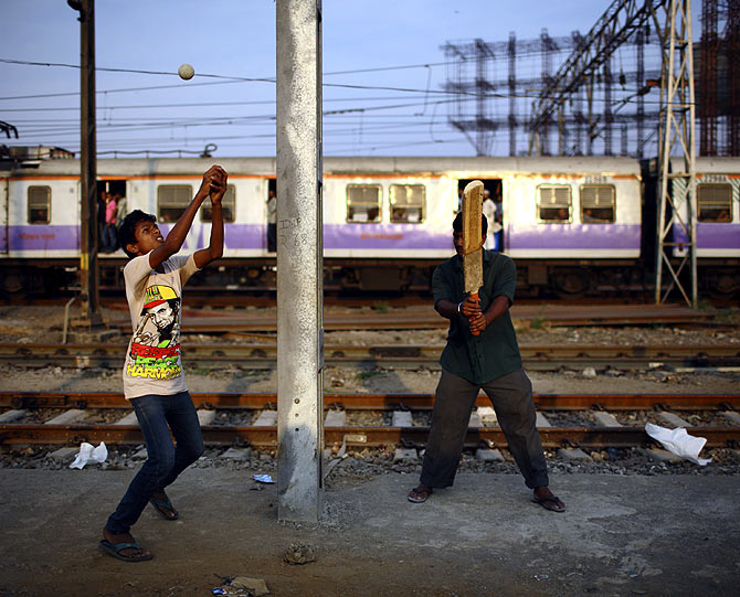Boys play cricket along the tracks as a local train passes by in Mumbai