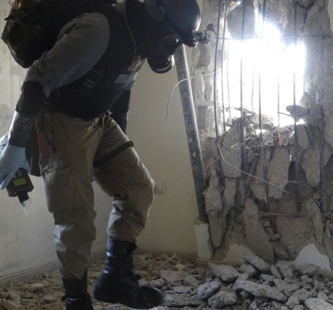 A UN chemical weapons expert, wearing a gas mask, inspects one of the sites of an alleged chemical weapons attack in the Damascus' suburb of Zamalka