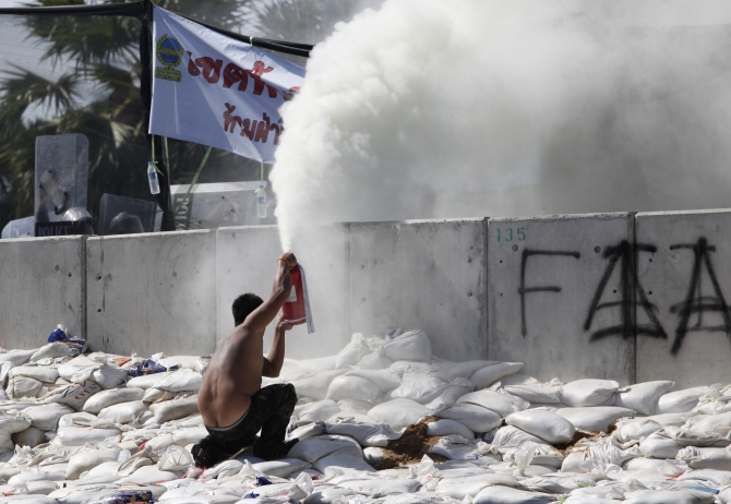 An anti-government protester uses a fire extinguisher during clashes with police near the Government House in Bangkok