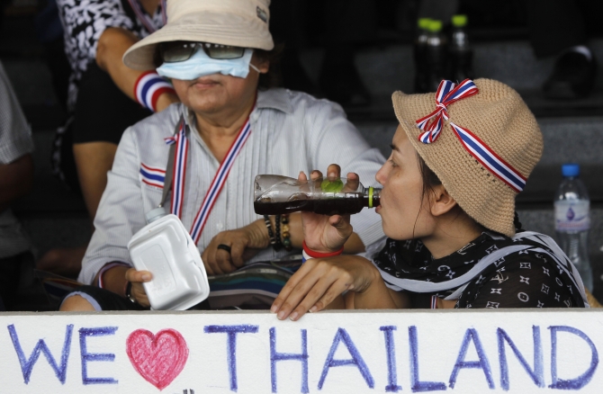An anti-government protester drinks coffee while holding a sign during a rally at a government complex in Bangkok
