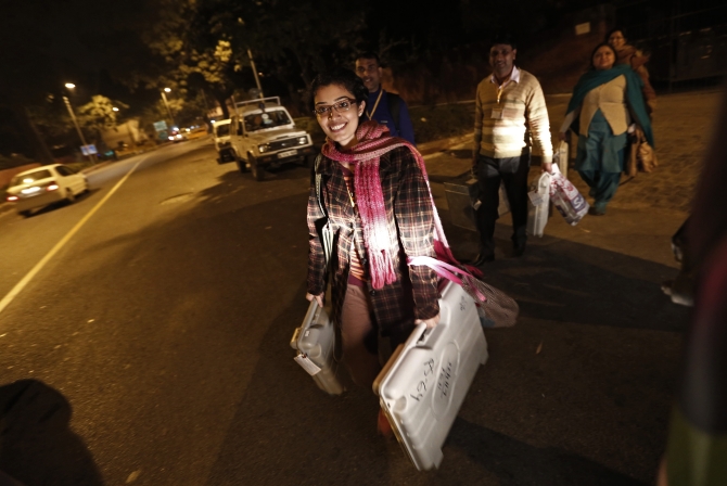 Polling officers carry electronic voting machines as they leave a polling station at the end of polls, during the state assembly election in New Delhi