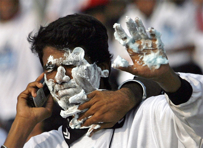 A man speaks on a mobile phone as another playfully applies shaving cream