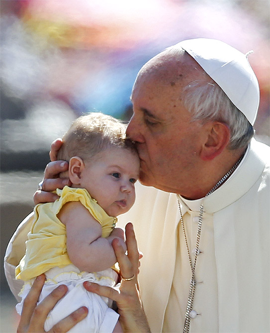 Pope Francis kisses a baby as he arrives to lead the weekly audience in Saint Peter's Square at the Vatican