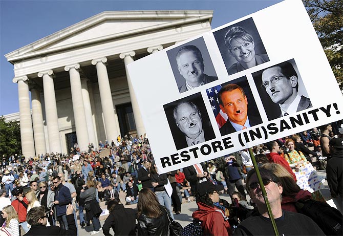 A man holds a placard portraying prominent conservatives including Rush Limbaugh with with 'Hitler moustaches'