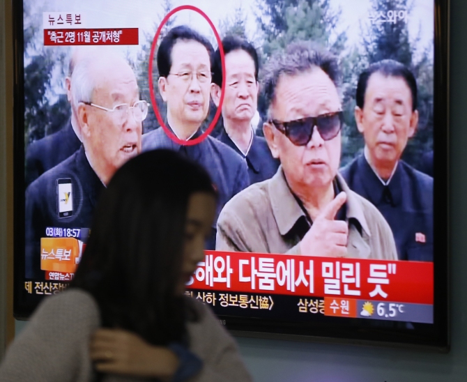 A woman walks past a television showing a report on Jang Song Thaek at a railway station in Seoul