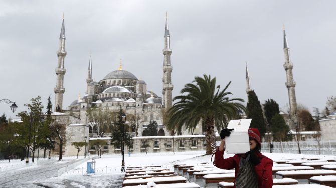 A foreign tourist, with the Ottoman-era Sultanahmet mosque, known as the Blue mosque in the background, takes souvenir photos as she strolls in snow-covered Sultanahmet square in Istanbul