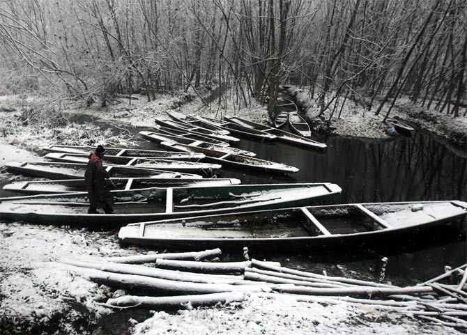 A Kashmiri man walks over snow covered parked boats