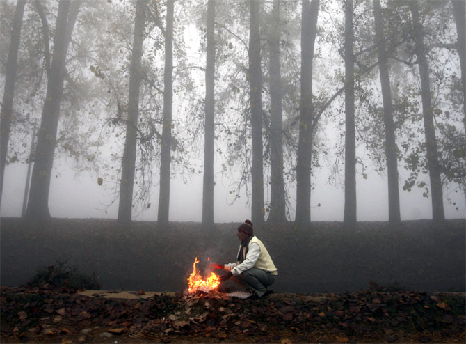 A man warms by a fire along a canal in Jammu