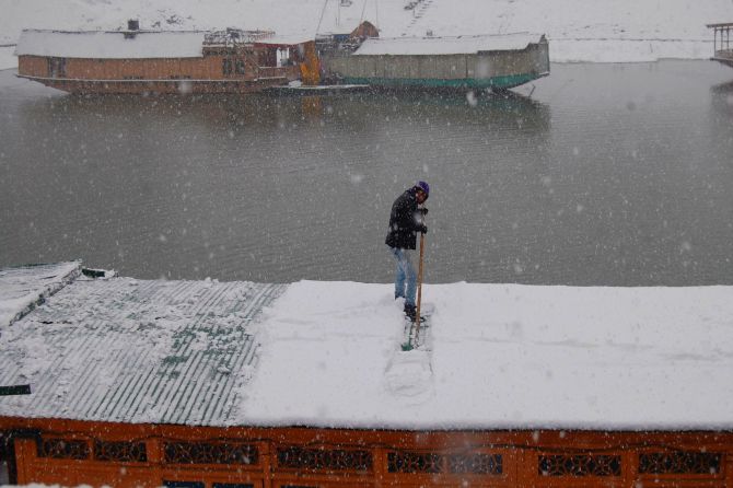 A man clears snow on the roof of a houseboat on Dal Lake on Tuesday