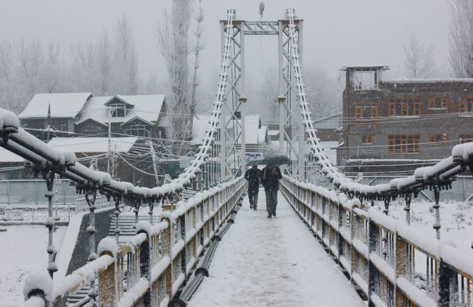 People walk on a snow covered bridge during heavy snowfall in Srinagar on Tuesday