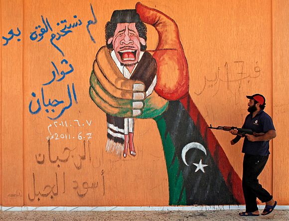 File photo of a Libyan rebel fighter walking past a graffiti depicting Muammar Gaddafi at a checkpoint near Yafran in western Libya