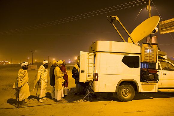Hindu devotees line up to see the ongoings inside of a TV satelite truck parked on the banks of the Ganga