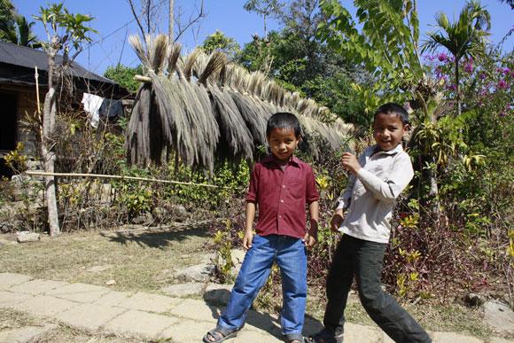 Children outside a home, behind a line of brooms ready to be sold.