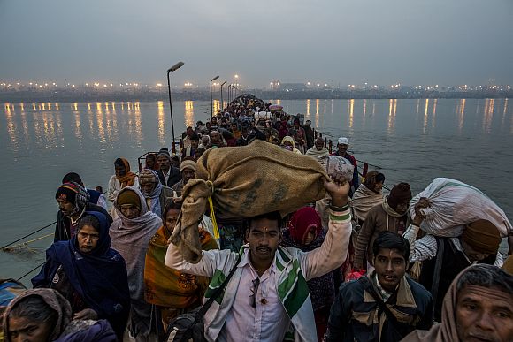Pilgrims walk across a pontoon bridge as others bathe on the banks of Sangam