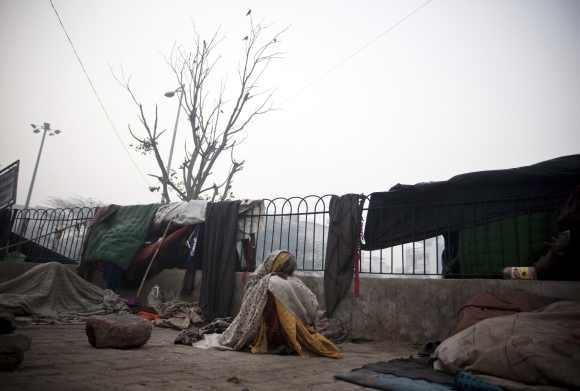 A homeless woman sits on a chilly morning beside a main road in New Delhi