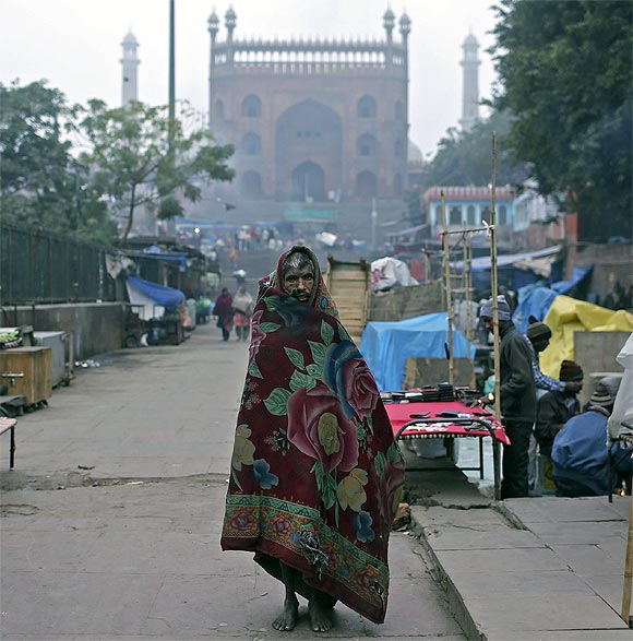 A man wrapped up in a quilt walks in front of the Jama Masjid