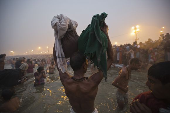A devotee holds his belongings aloft as he attends the first Shahi Snan at the ongoing Kumbh Mela in Allahabad