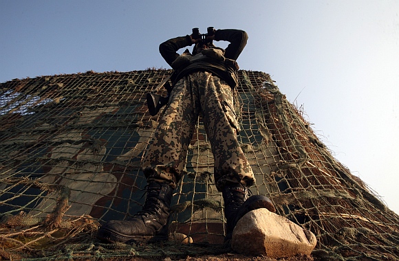 A Border Security Force soldier looks through a pair of binoculars outside a bunker near the fenced border with Pakistan in Suchetgarh, southwest of Jammu