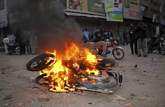 A man rides past burning motorbikes, which were burnt by supporters of Pakistan People's Party to protest against a Supreme Court decision to arrest Prime Minister Raja Pervez Ashraf in Larkana