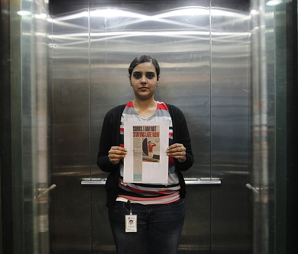 Deepshikha poses inside her office elevator holding a notice that reads 'sorry I am not staying late now' in her office in Gurgaon on the outskirts of New Delhi