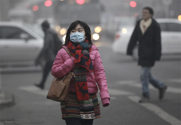 A woman wearing a mask walks along a street on a hazy day in Beijing