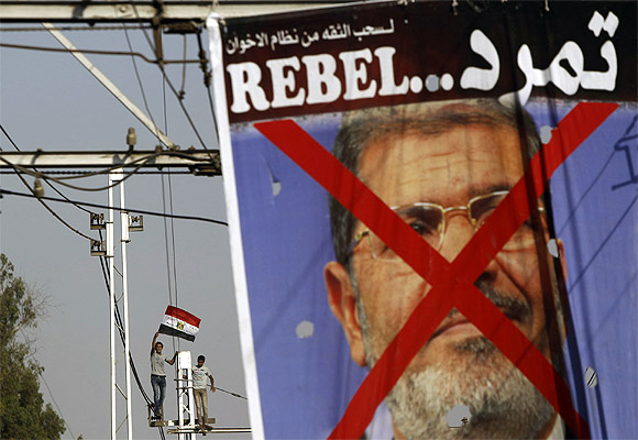 Protesters opposing Mursi stand on top of an electric tram column and wave Egyptian flags during a protest in front of El-Thadiya presidential palace in Cairo