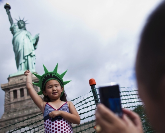 A girl poses for her father as they visit the Statue of Liberty and Liberty Island during its reopening to the public in New York, July 4,