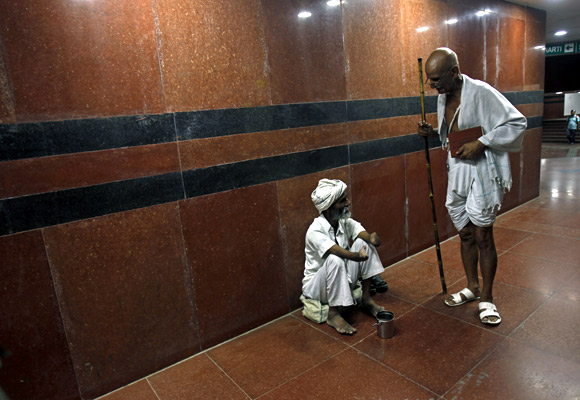 A man dressed like Mahatma Gandhi talks to a beggar while walking through a Delhi subway