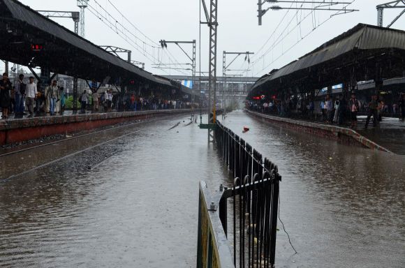 Commuters wait for trains as rain water inundates tracks at Thane station on Friday