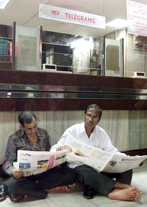 Telecom workers read newspapers in front of their counters in Mumbai