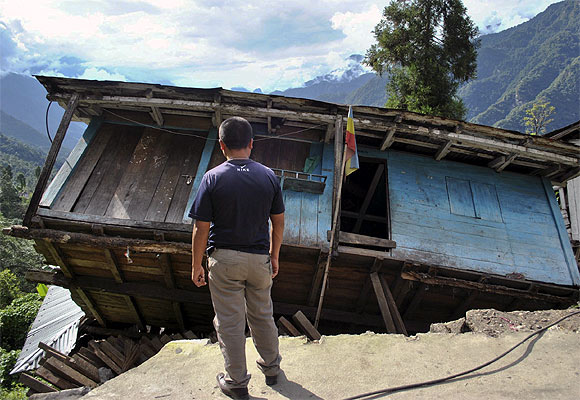 A man stands in front of his house, which was damaged by an earthquake