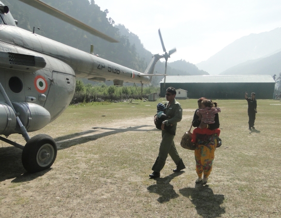 An IAF trooper helps a lady and child into a helicopter.