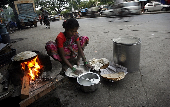 A woman cooks food on a street in front of her shanty in Mumbai
