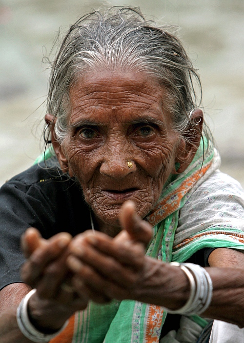 An elderly homeless woman begs on a street in New Delhi