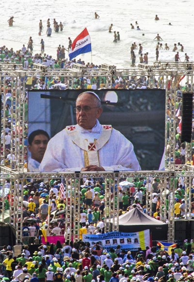 Pilgrims watch Pope Francis on a video screen as he celebrates mass on Copacabana Beach in Rio de Janeiro.