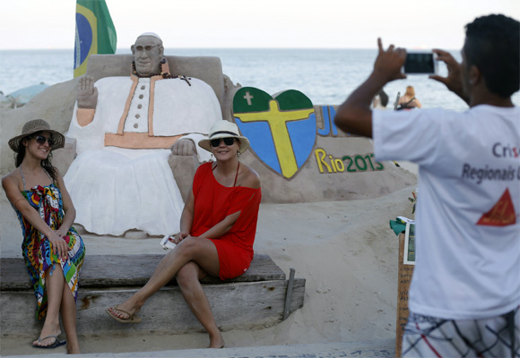 Artist Rogean Rodrigues takes pictures for tourists in front of his Pope Francis sand sculpture.