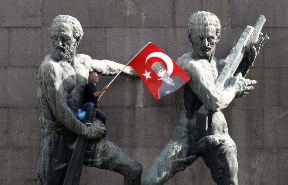 A demonstrator waves Turkey's national flag as he sits on a monument during a protest against Turkey's Prime Minister Tayyip Erdogan and his ruling AK Party in central Ankara